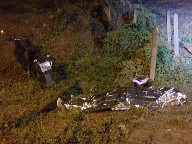 Na imagem vemos a motocicleta preta em pé. Ao lado dela está o corpo do homem coberto por uma manta térmica. Na imagem vemos a motocicleta preta em pé. Ao lado dela está o corpo do homem coberto por uma manta térmica.