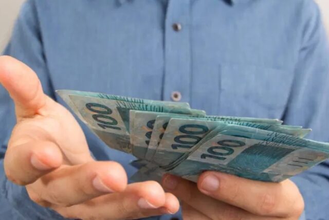 Uma foto de um homem segurando cédulas de 100 reais