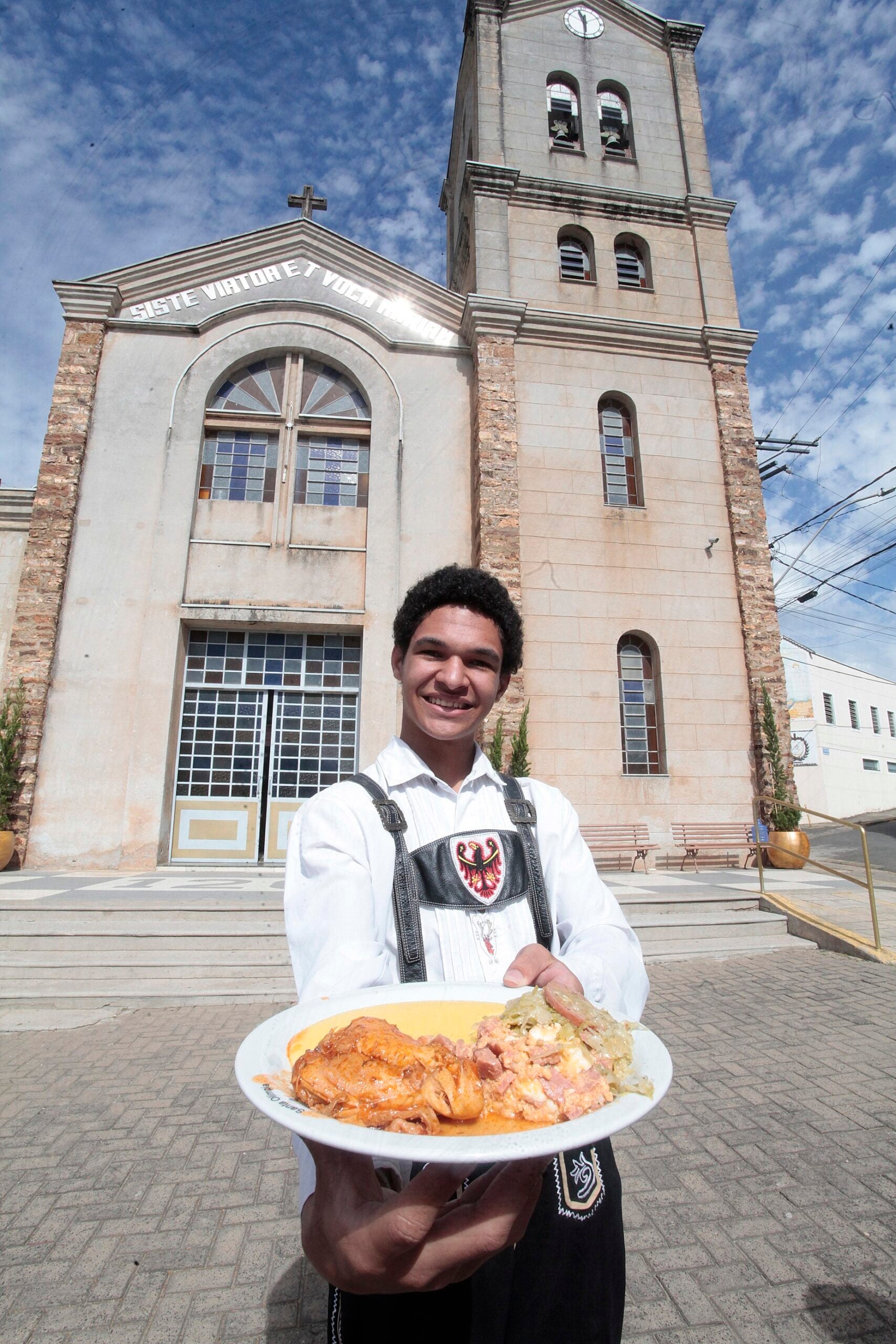 Luis Forti Pompermayer apresenta prato típico da Festa da Polenta diante da igreja de Santa Olímpia